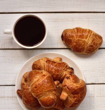 bir fincan kahve ve bir plaka ile beyaz bir retro ahşap masa üzerinde altın kabuk ile taze pişmiş kruvasanlar, yakın çekim. Kahve zamanı. kahve ruh hali. 