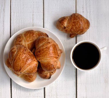 bir fincan kahve ve bir plaka ile beyaz bir retro ahşap masa üzerinde altın kabuk ile taze pişmiş kruvasanlar, yakın çekim. Kahve zamanı. kahve ruh hali. 