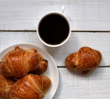 bir fincan kahve ve bir plaka ile beyaz bir retro ahşap masa üzerinde altın kabuk ile taze pişmiş kruvasanlar, yakın çekim. Kahve zamanı. kahve ruh hali. 