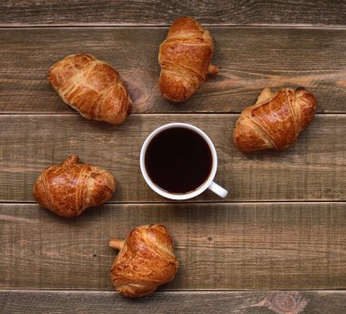 bir fincan sade kahve ve taze pişmiş kruvasanlar bir kahverengi ahşap masa üzerinde altın kabuk ile. kahve ruh. kahve saati.  