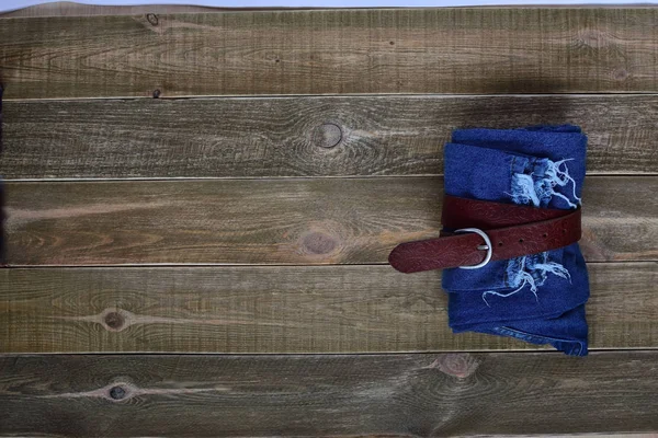 top view of high waist women  blue folded jeans and a leather belt on brown wooden background. teens concept. teenager.