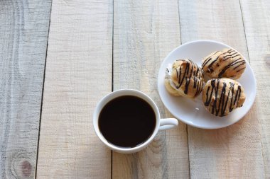 Kahve zamanı. kahve ruh. tatlı zamanı. metin için yer. Ahşap arka plan üzerinde fincan kahve ve bir tabak doldurma ve çikolata kremalı profiterol ile kaplı . 