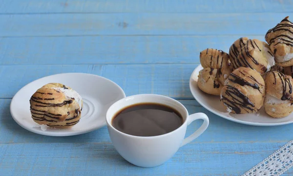 coffee time. coffee mood. sweet time.  Cup of coffee and a plate with profiterole with cream filling and chocolate covered on a blue wooden background decorated with retro rustic lace.