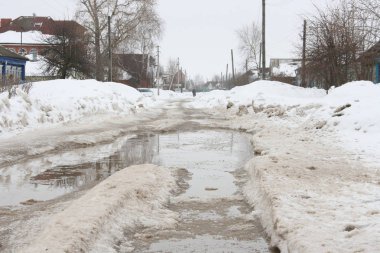 Büyük su birikintileri ve yüksek kar yığınları ile erken baharda köyde yol