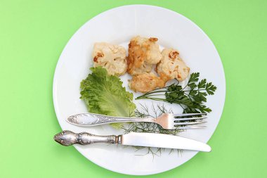 Marul, maydanoz ve yeşil bir arka plan üzerinde bir bıçak ve çatal ile beyaz bir tabak taveotu bir sprig ile meyilli karnabahar