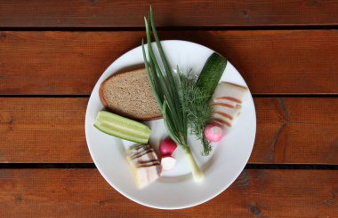 Tuzlu pastırma, çavdar ekmeği ve taze sebzeler, yeşil soğan, kırmızı turp, yeşil dereotu, kahverengi ahşap bir masa üzerinde bir tabak salatalık