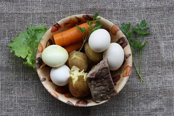 Boiled potatoes, meat, carrots in a plate on a background of coarse cloth