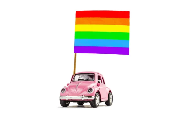 Carro de brinquedo retro rosa entregando bandeira gay arco-íris brilhante. Conceito de parada gay, comunidade LGBT, adoção e direitos humanos. Isolado em branco. Foco suave — Fotografia de Stock