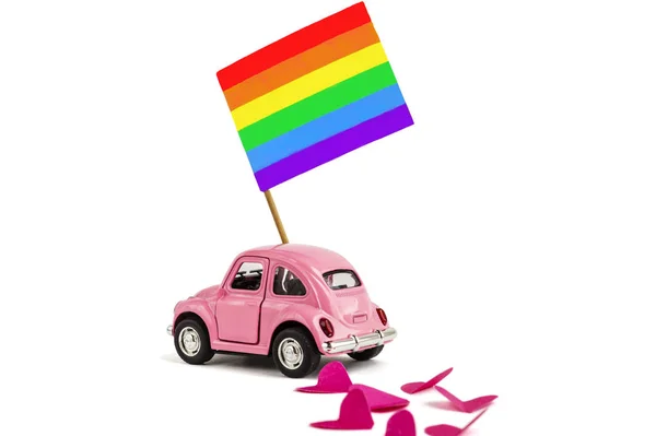 Pink retro toy car delivering bright rainbow gay flag. Concept of gay parade, LGBT community and human rights. A car leaves a love mark in the form of hearts. Isolated on white — Stock Photo, Image