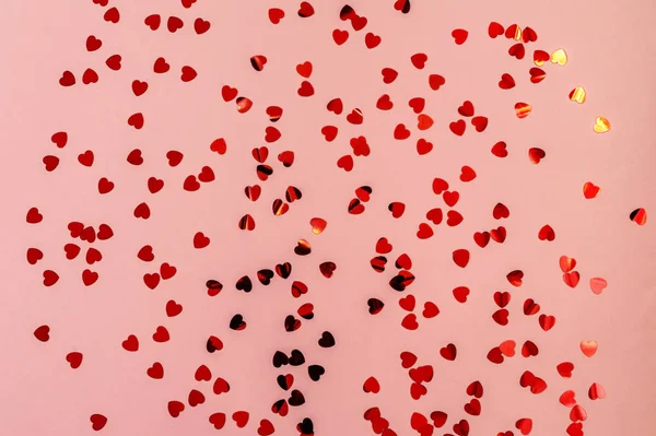 Czerwone świecące konfetti w kształcie serca na różowym tle pastelowych. Świąteczne tło wakacyjne dla Twoich projektów — Zdjęcie stockowe