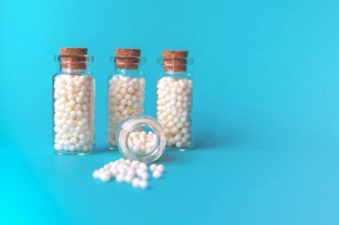 Mavi arka planda dört cam şişe Homeopatik globüller. Globüller bir şişeden dağılmış durumdadır. Alternatif Homeopati tıp otlar, sağlık ve haplar kavramı. Seçici odak