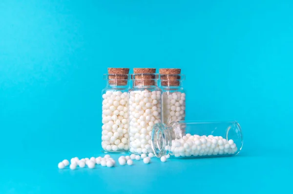 Mavi arka planda dört cam şişe Homeopatik globüller. Globüller bir şişeden dağılmış durumdadır. Alternatif Homeopati tıp otlar, sağlık ve haplar kavramı. Metin için boşluk Kopyala