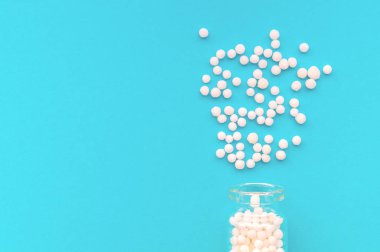 Pastel mavi arka plan üzerinde cam şişe homeopatik globüller. Globüller şişeden saçılmış. Alternatif homeopati ilaç otlar, sağlık ve hap kavramı. Seçici odaklama