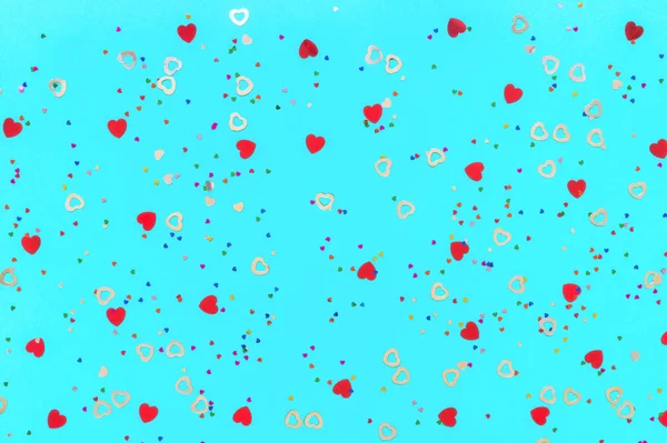 Zdjęcie konfetti w kształcie serca różnych rozmiarów i kolorów posypuje na niebieskim tle. Świąteczne tło wakacji dla Twoich projektów. Koncepcja obchodów. Wzór świąteczny. Widok z góry — Zdjęcie stockowe