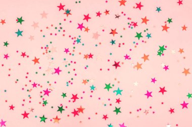 Çok renkli yıldızların soyut fotoğrafı pembe arka planda parlıyor. Şenlikli tatil pastel fon. Kutlama konsepti. Üst görünüm, düz yatıyordu. Yatay