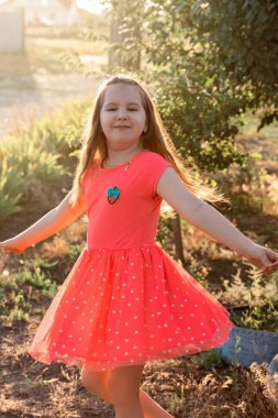 Kırmızı elbiseli, uzun saçlı güzel, gülümseyen küçük kız gün batımında döner..