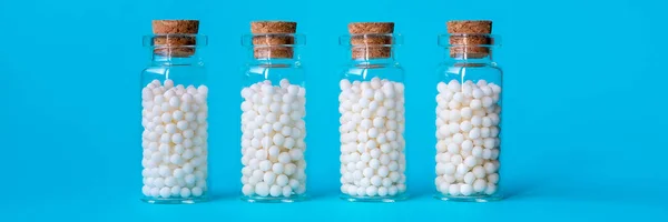 Banner image of homeopathic globules in glass bottles on pastel blue background.