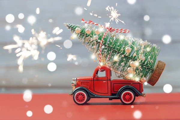 Işıl ışıl parlayan bokeh ve havai fişekleri olan küçük kırmızı oyuncak kamyon, kırmızı ve gri arka planda, kamyon gövdesine Noel ağacı bırakıyor. Teslimat, Noel, yeni yıl konsepti. Boşluğu kopyala.