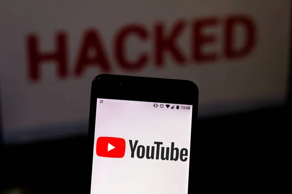 16 августа 2019 года, Бразилия. На этой фотографии логотип YouTube отображается на смартфоне и красном предупреждающем слове HACKED на размытом фоне. Концептуальное фото для нарушения данных — стоковое фото