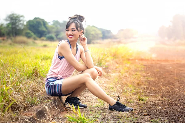 Fitness model in sportswear sitting on the sidewalk with blurred background at dusk. Outdoor sports clothing, urban style. Copy space for text — Stock Photo, Image