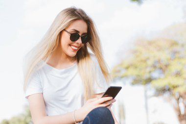 Modern genç kadın büyük şehir meydanında akıllı telefon kullanarak - Genç şık hipster sosyal ağlarda arkadaşlarıyla konuşurken onu güneş gözlüğü ile kaygısız gülümseyen. Teknoloji Kavramı. Yaşam tarzı