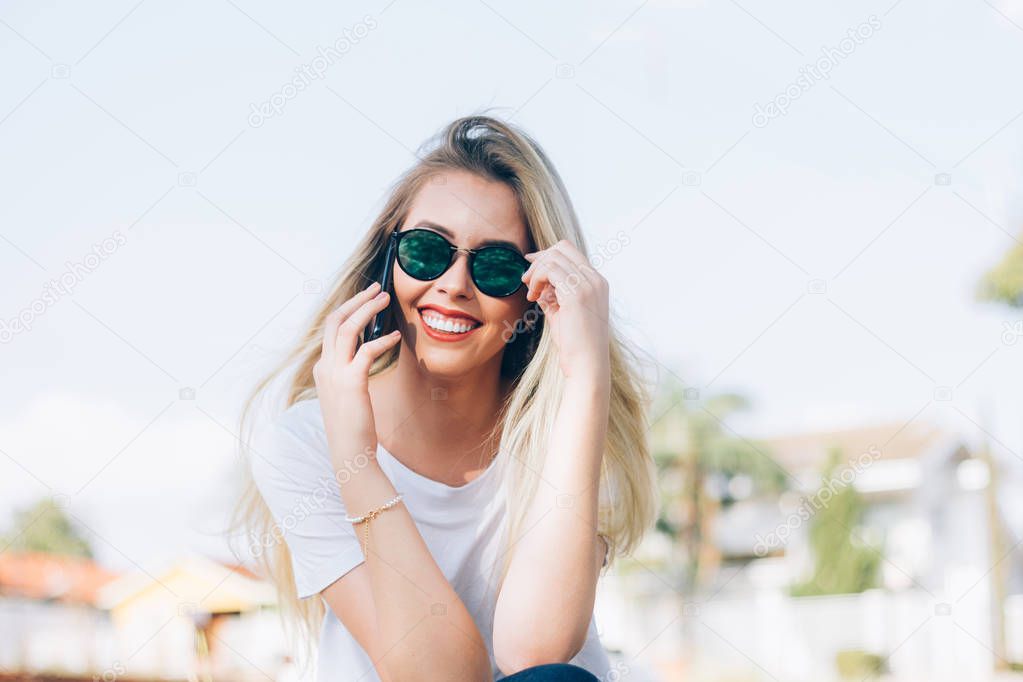 Modern young woman using her smartphone - Young stylish hipster smiling carefree with her sunglasses and talking with her friends over the phone. Fashion, trendy and millennial generation concept