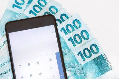 Brezilya parası - 100 reais banknot ve hesap makineli akıllı telefon - ekonomik konsept - enflasyon ve iş dünyası.