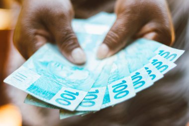 Brezilya parası sergileyen zenci bir kadının eli - Yüz Brezilyalı Reais banknotları - Ekonomi kavramı - enflasyon ve iş dünyası.