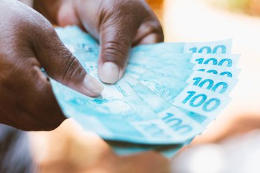 Brezilya parası sergileyen zenci bir kadının eli - Yüz Brezilyalı Reais banknotları - Ekonomi kavramı - enflasyon ve iş dünyası.
