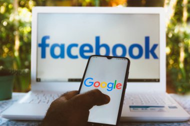 7 Haziran 2020, Brezilya. Bu resimde Google logosu bir akıllı telefonda gösteriliyor. Arka plandaki bilgisayar ekranında Facebook logosu.