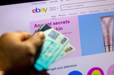 5 Temmuz 20020, Brezilya. eBay web sitesi arka planda bir dizüstü bilgisayarda gösteriliyor ve bir kişinin elinde bir banka kartı bulunuyor