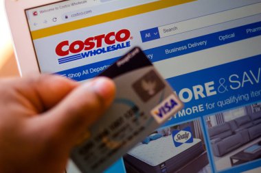 5 Temmuz 20020, Brezilya. Costco Toptan Şirketi 'nin web sitesi arka planda bir dizüstü bilgisayarda gösteriliyor ve bir kişi banka kartı tutuyor.