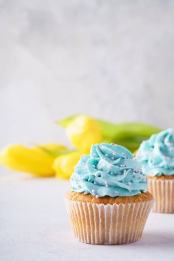 Mavi buzlanma ve arka planda sarı çiçekleri ile vanilya cupcakes. Anneler günü veya doğum günü tatlı.