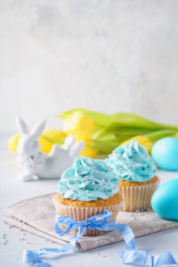 Ev yapımı vanilyalı kek sprinkles ve mavi kurdele ile süslenmiş. Bunny, renkli yumurta ve arka planda Sarı laleler.