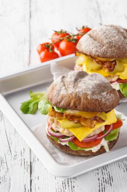 Tam tahıllı tavuk veya hindi, marul, domates ve pastırma çizburger. Beyaz ahşap zemin.