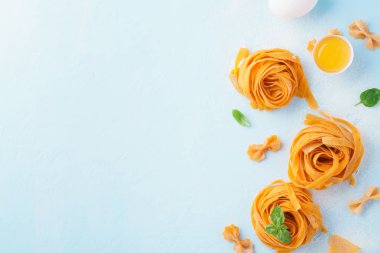 Taze çiğ ev yapımı makarna tagliatelle veya fettuccine yumurta sarısı, kabuk ve fesleğen açık mavi renkli üzerinde. Boşaltmak, üstten görünüm.