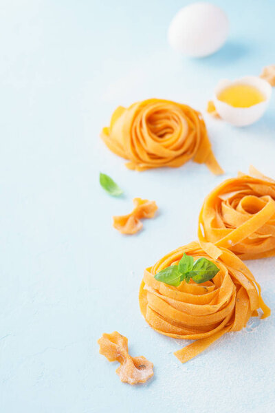 Fresh raw uncooked homemade pasta fettuccine with egg yolk and shell over light blue background.