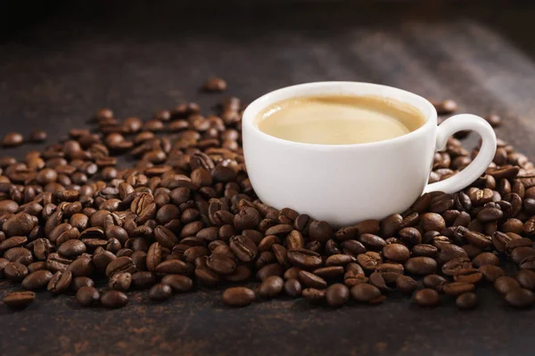 Kahve fincanı kavrulmuş kahve çekirdeği üzerinde. Koyu arka plan, güneş ışınları.