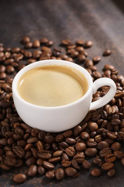Xícara de café em grãos de café torrados. Fundo escuro, raios de sol . — Fotografia de Stock