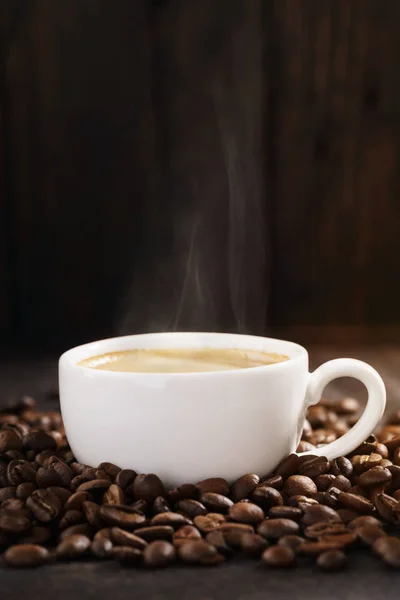 Xícara de café quente com vapor e grãos de café torrados . — Fotografia de Stock