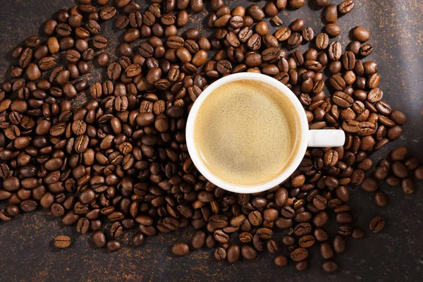 Kahve fincanı kavrulmuş kahve çekirdeği üzerinde. Koyu arka plan, güneş ışınları.