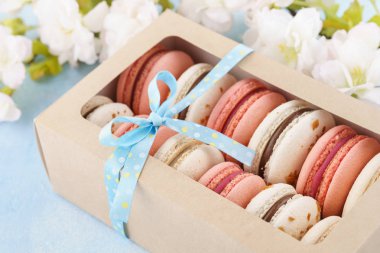 Mavi arka planda şerit ve çiçekler ile bir kutuda macarons.