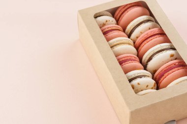 Pembe arka planda bir hediye kutusunda renkli Makaron.