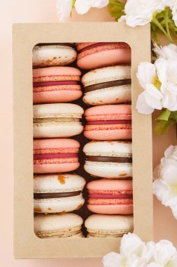 Pembe arka planda bir kutu ve çiçekler macarons.