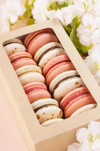 Pembe arka planda bir kutu ve çiçekler macarons.