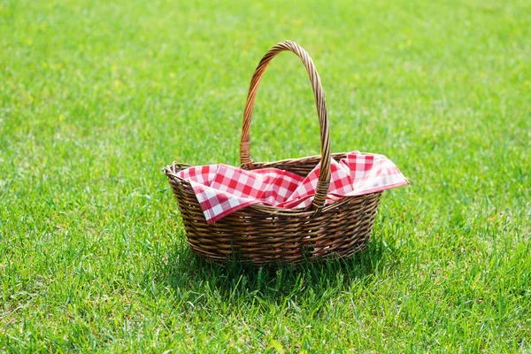 Empty wicker basket with red tablecloth on green grass in a park