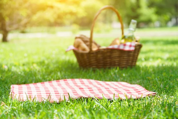 Wicker picnic basket with food and red tablecloth on the grass. — Stock Photo, Image