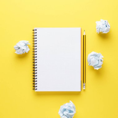 Açık defter, kalem ve buruşturulmuş kağıtları sarı arka plan üzerinde.