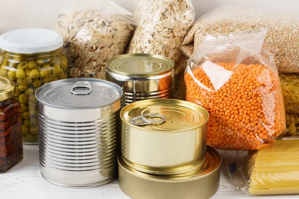 Various canned food and raw cereal grains on a table. — Stock Photo, Image