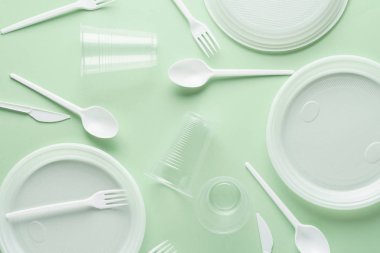 Yeşil arka plan üzerinde çeşitli beyaz plastik tek kullanımlık sofra.